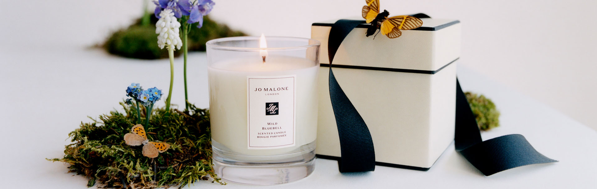image of a cologne in a jo malone cream & black box with candles on a marble table with flowers beside 