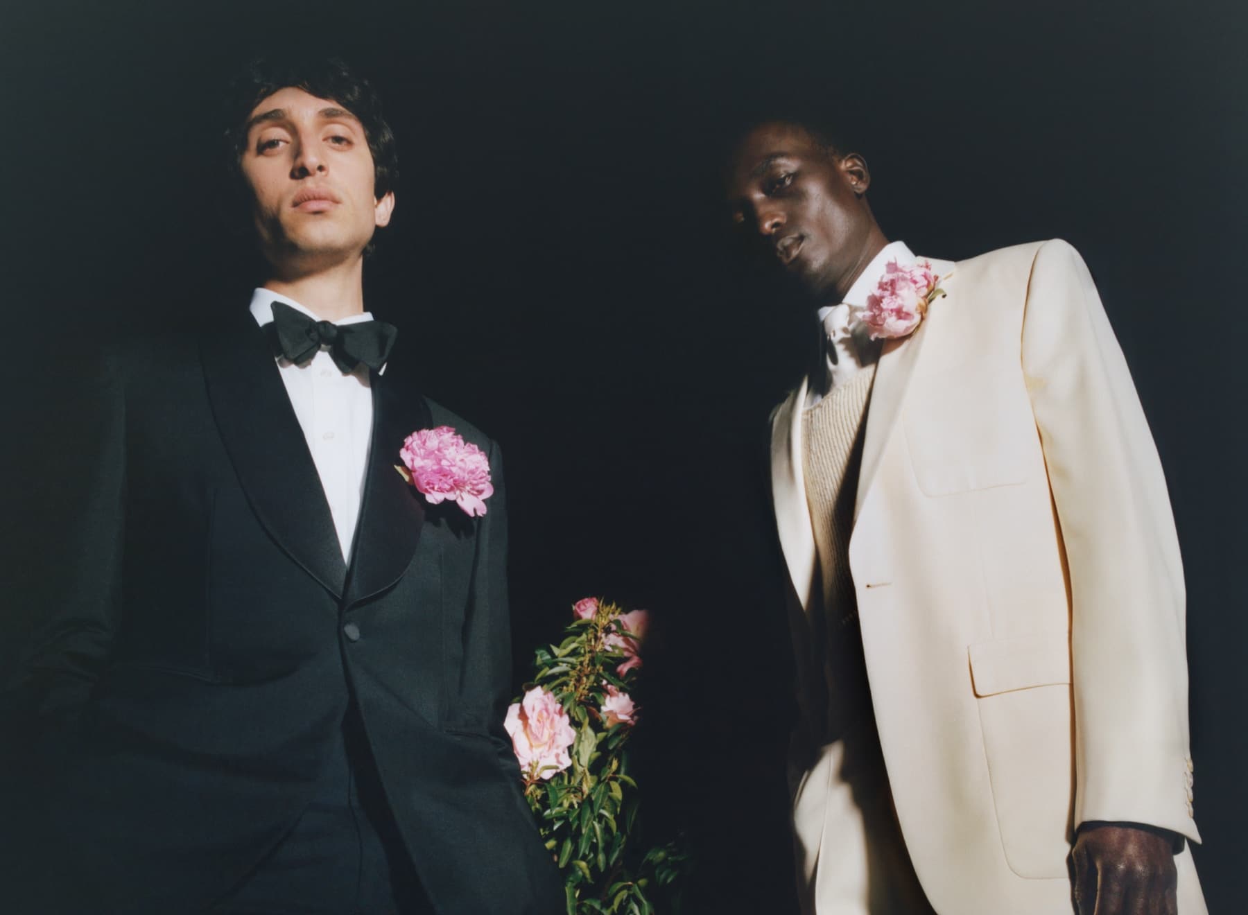 Two people, one wearing a black tux and the other a white tux with pink corsages shot at night from an upward angle.