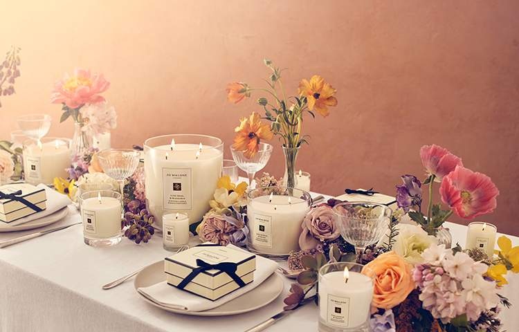 Image of a wedding dining table covered in colourful flowers & jo malone candles in different sizes for a scented wedding