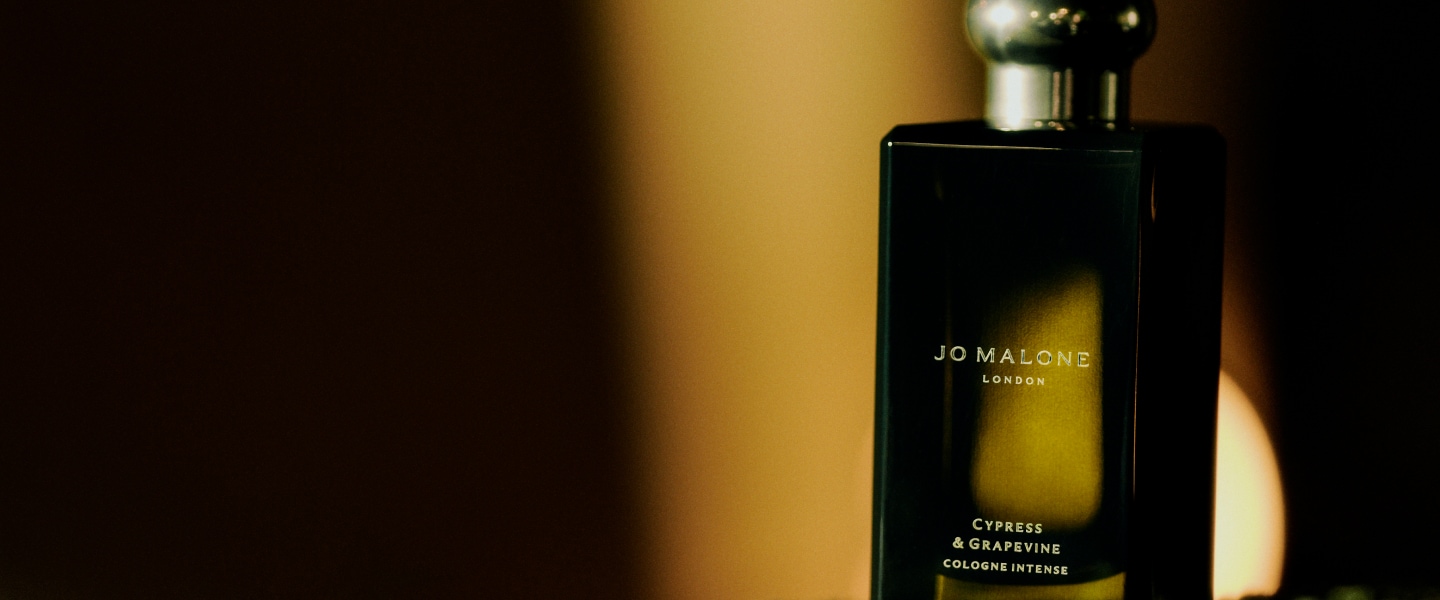 Jo Malone London Cypress and Grapevine cologne bottle sits against a dark background, atop a bed of grapevines.