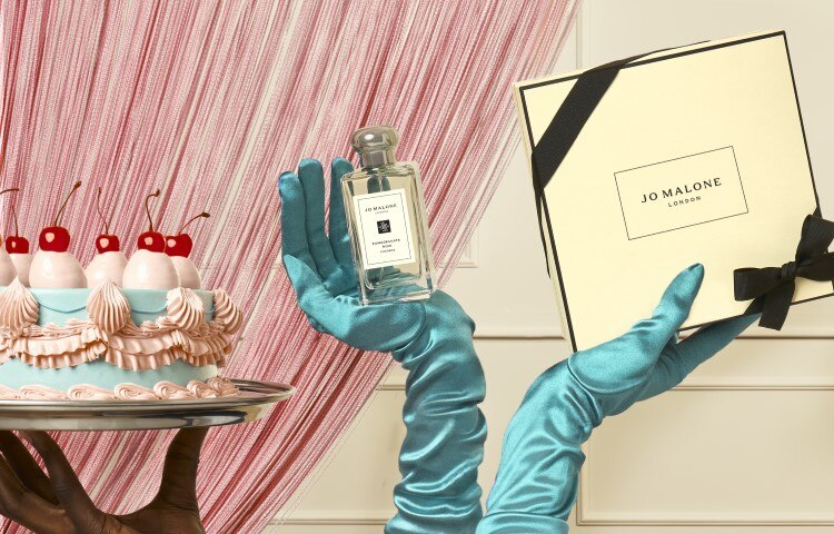 birthday cake & a pair of hands in satin green gloves holding jo malone gift bags, gift boxes, candle and diffuser