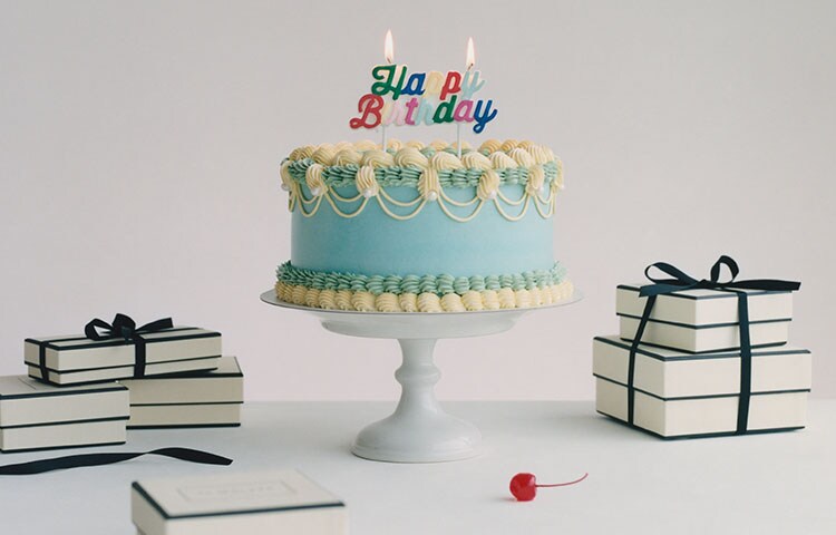 birthday cake & a pair of hands in satin green gloves holding jo malone gift bags, gift boxes, candle and diffuser