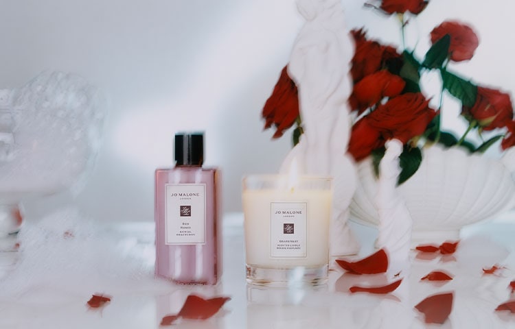 image of jo malone cream and black boxes stacked with a body creme balanced on top and flowers in a vase behind