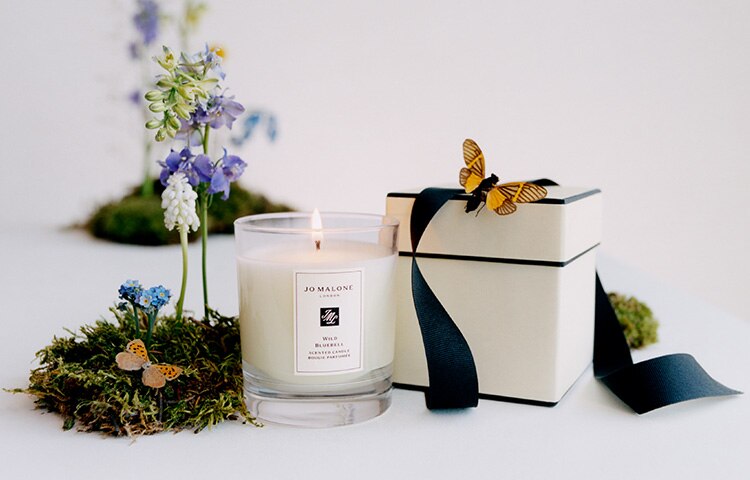 image of a cologne in a jo malone cream & black box with candles on a marble table with flowers beside 